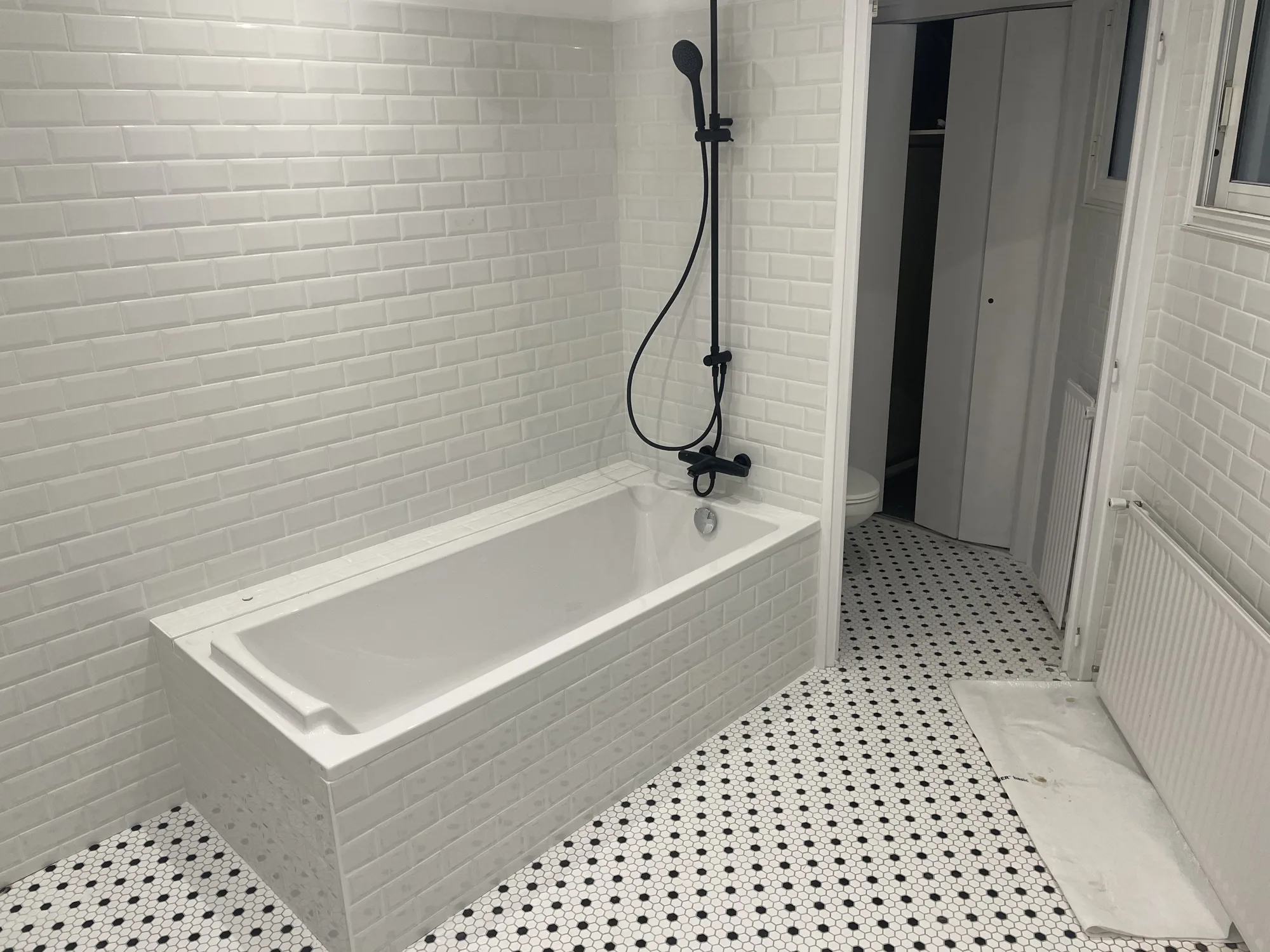 Salle de bains avec faience metro blanche, baignoire et sol en mosaique hexagonale noire et blanche, posee par un carreleur pres de Challans