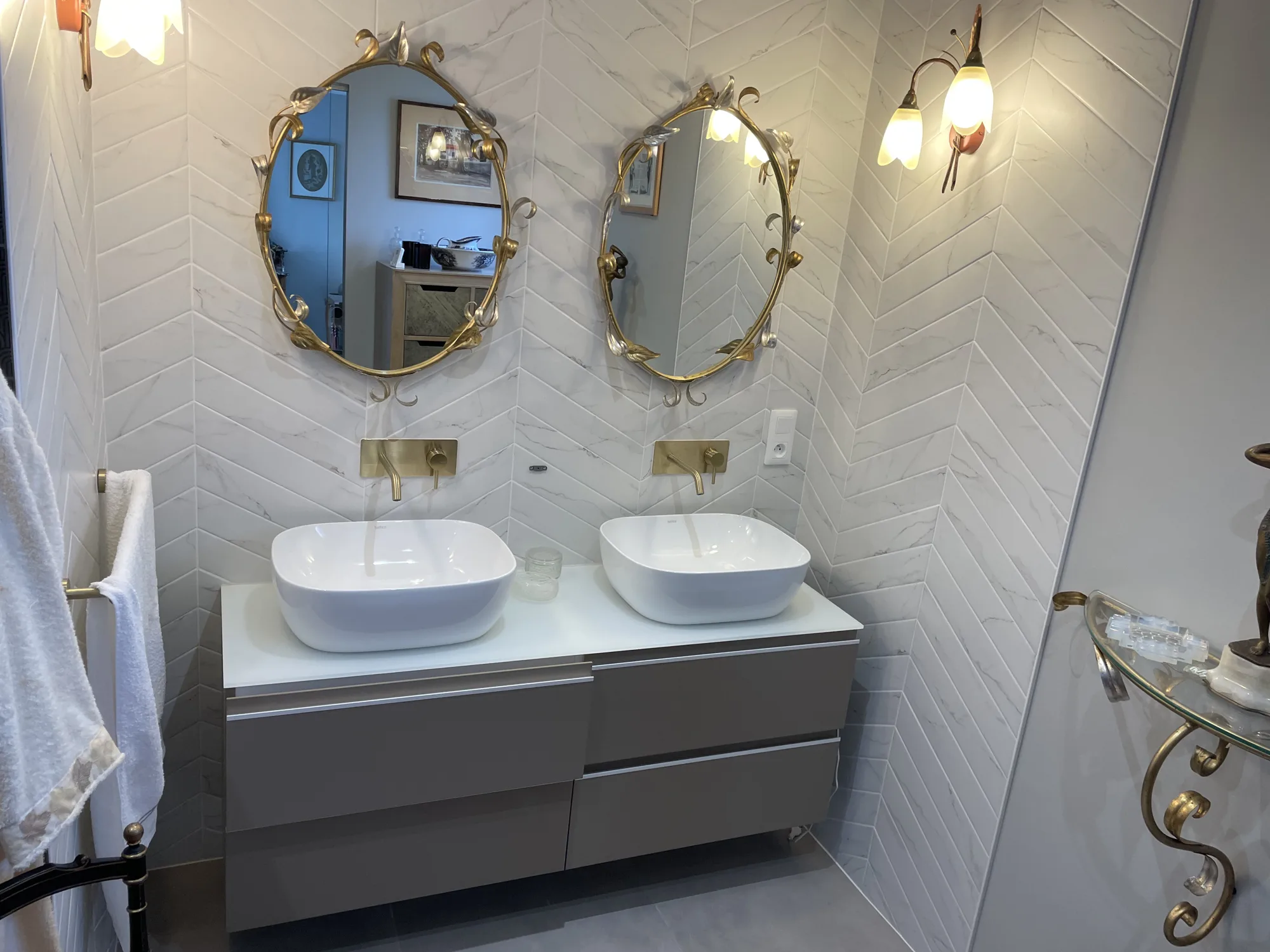 Salle de bains en faience blanche effet marbre posee en chevrons, double vasque et robinetterie doree, realisee par un carreleur en Vendee